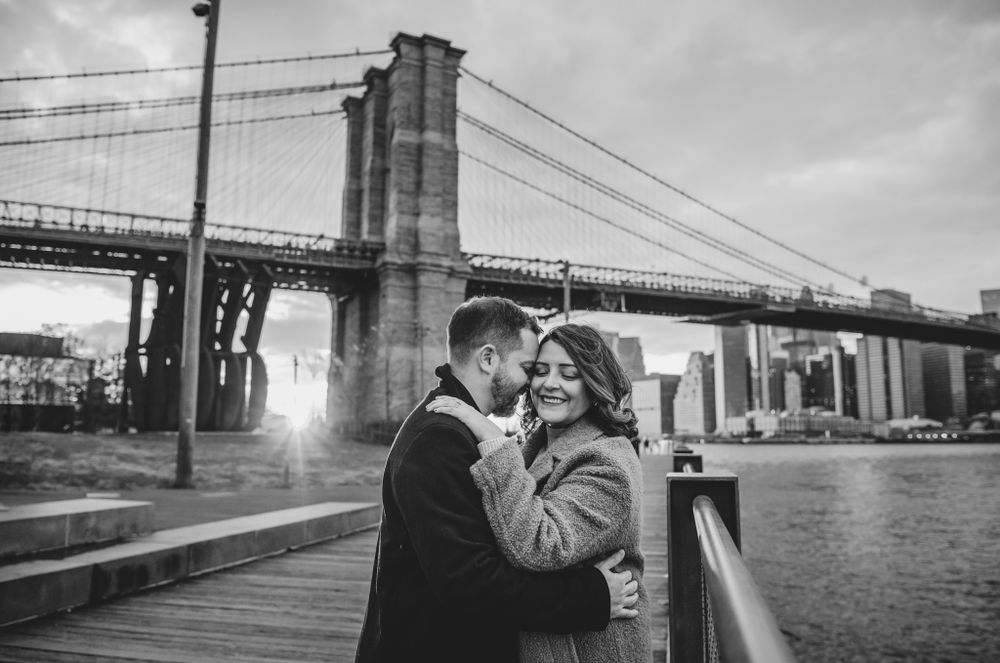 Couple embracing near Brooklyn Bridge during golden hour photoshoot.