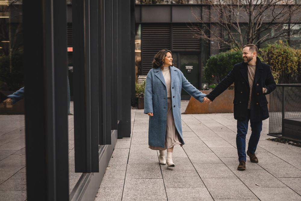 A couple in winter coats share an intimate moment on a modern urban walkway.