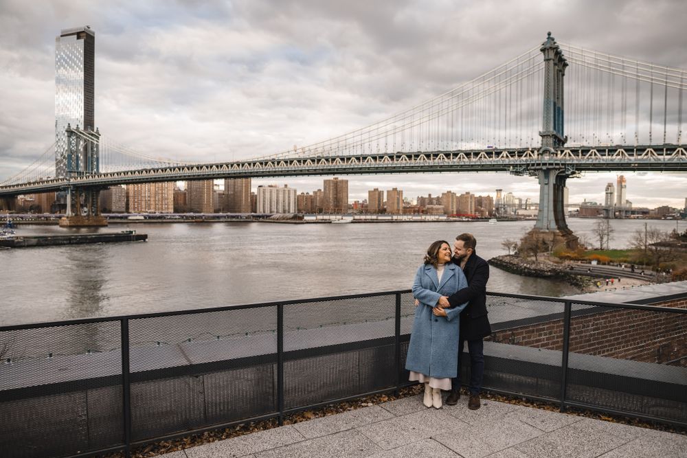 A cloudy waterfront view with urban architecture and bridge visible in the distance.
