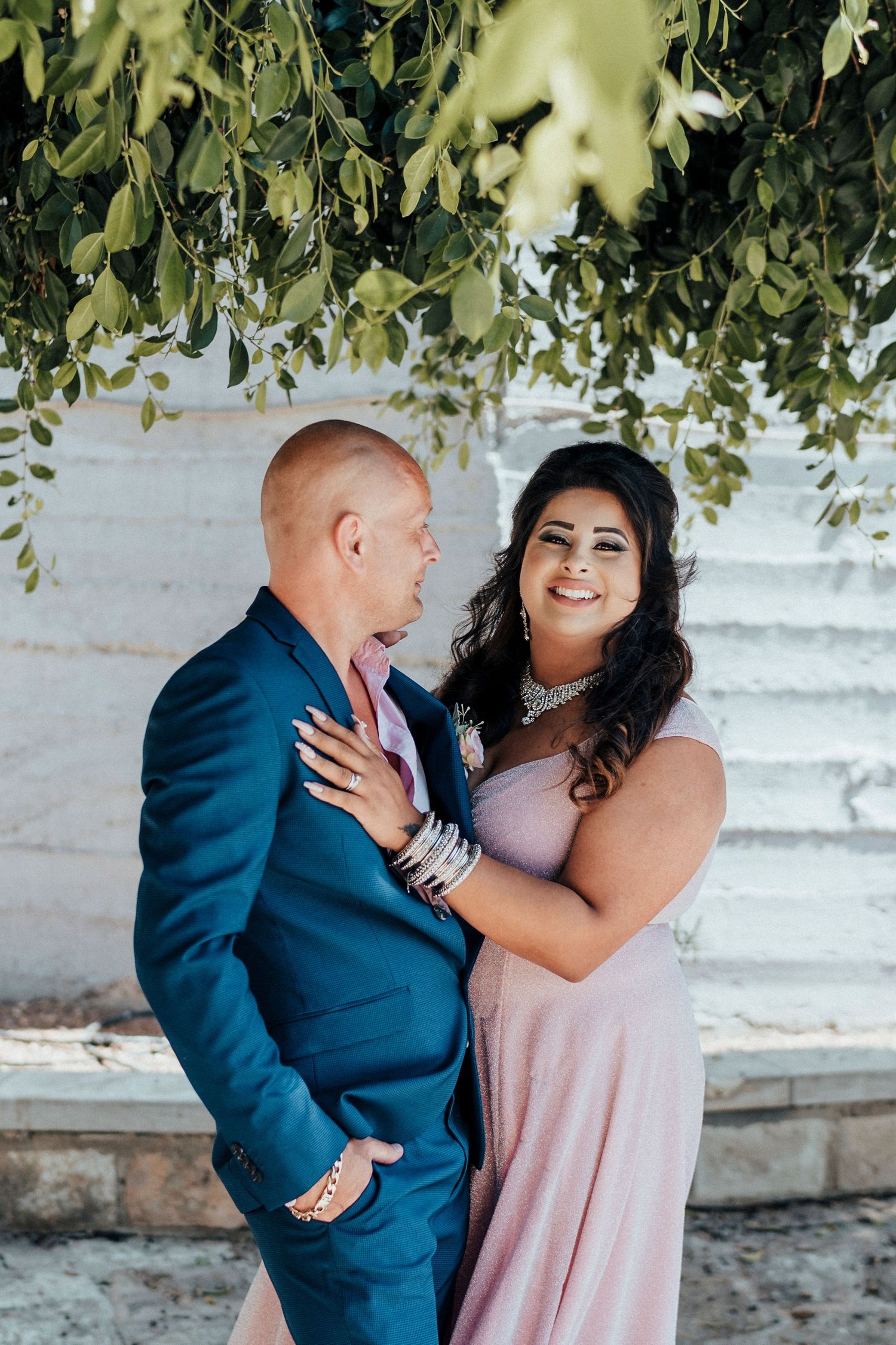 Happy couple sharing a joyful moment together under hanging foliage wearing formal attire.