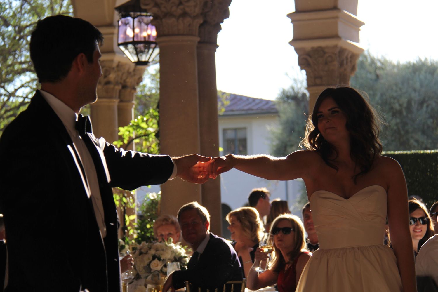 Wedding ceremony moment with couple exchanging rings under columned archway.