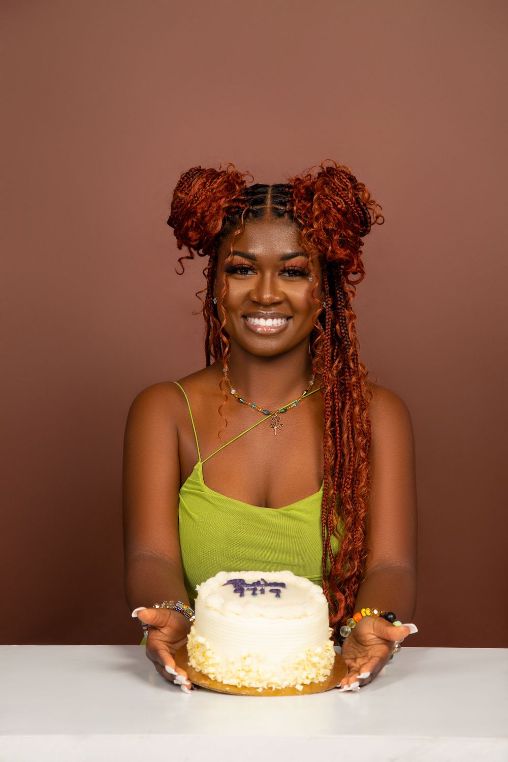 Portrait of person with red braided buns hairstyle presenting a white cake.
