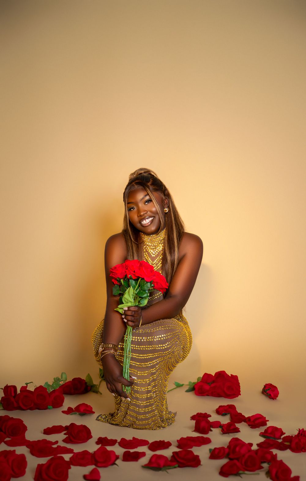 Glamour portrait with red roses and gold dress against beige background with scattered petals.