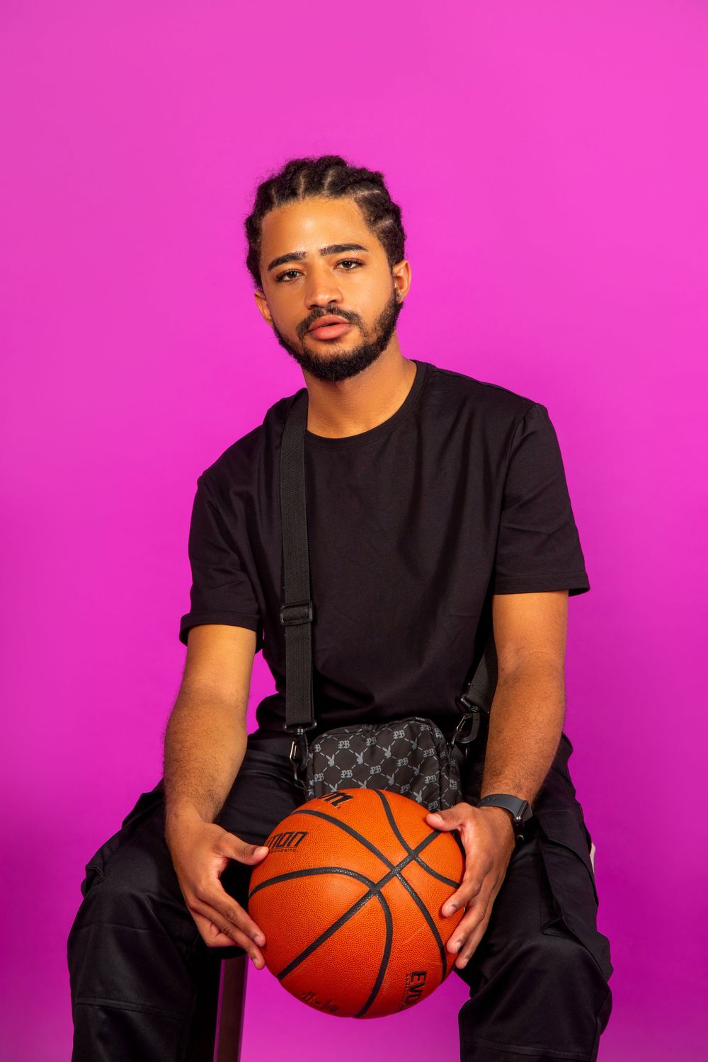 Portrait of person in black outfit holding basketball against pink background.
