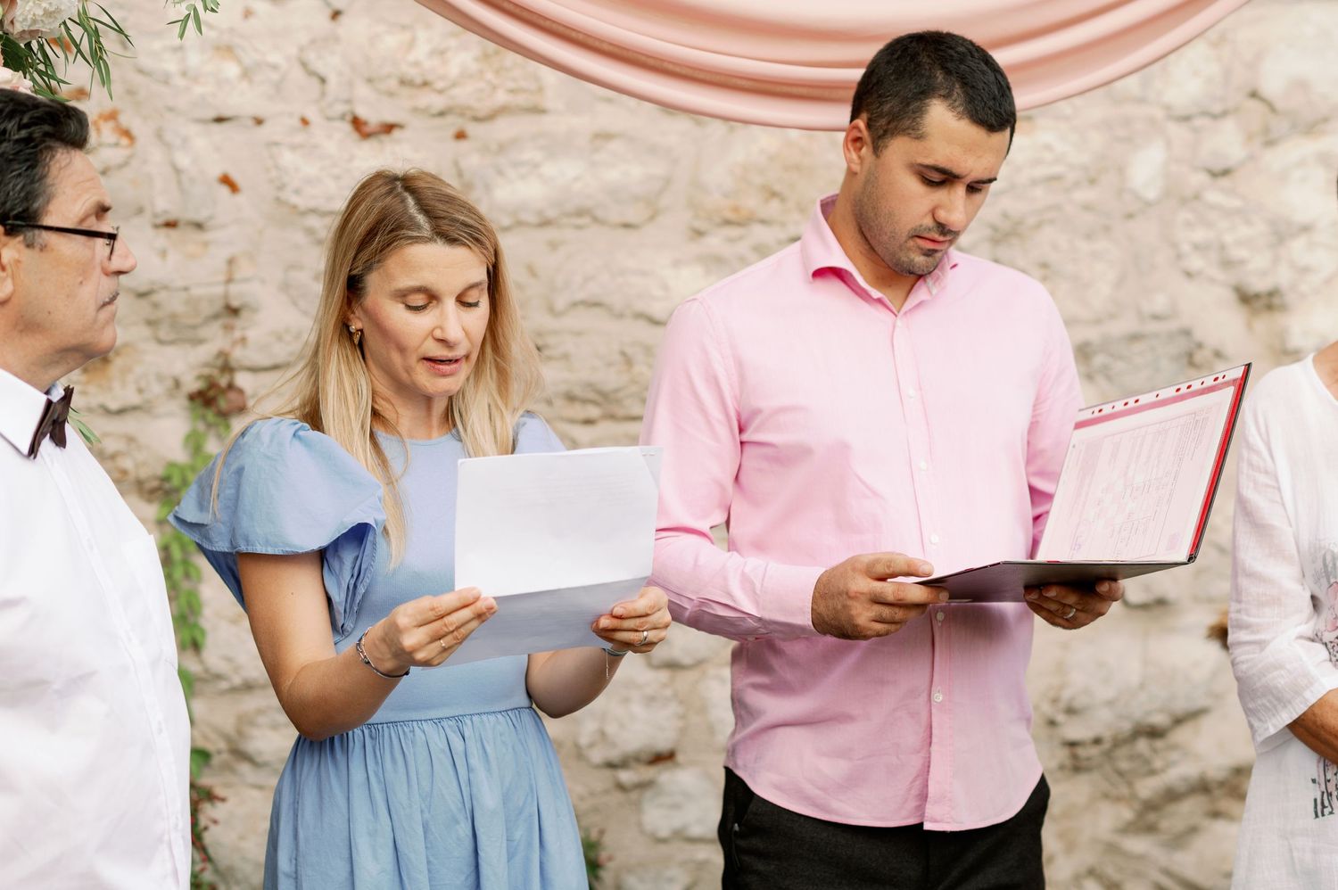 Wedding ceremony participants reading from documents during an outdoor service.