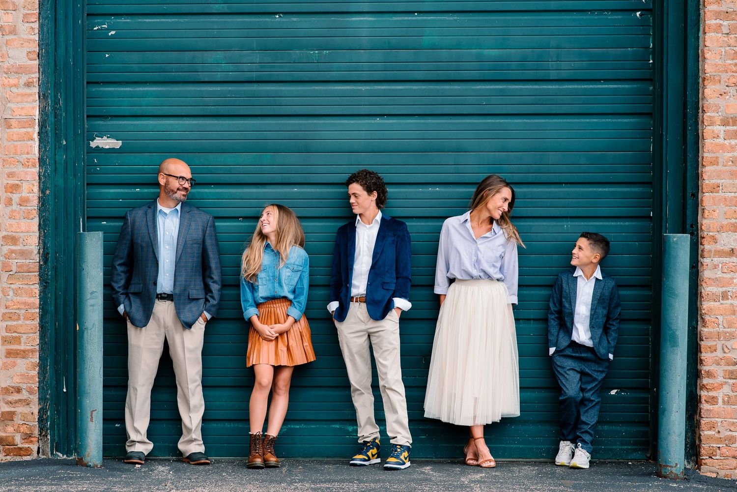 A group stands casually against a teal garage door wearing coordinated casual outfits in an urban setting.