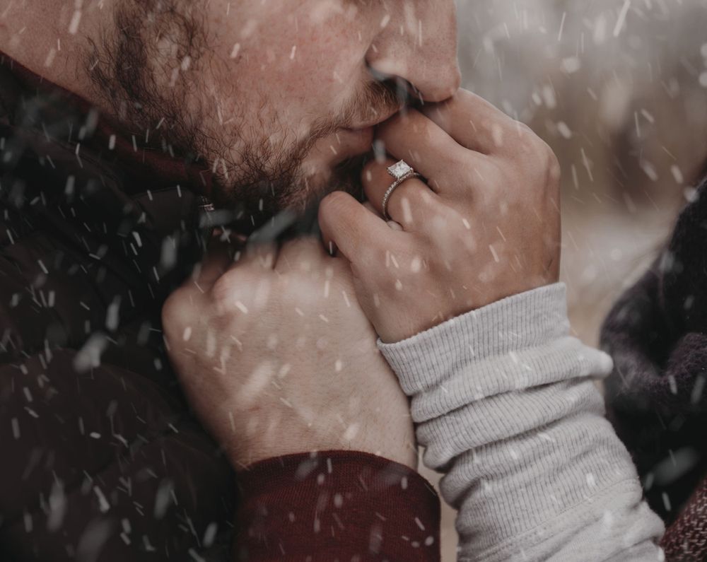 A close-up shot of hands touching in winter with snowflakes falling in the background.