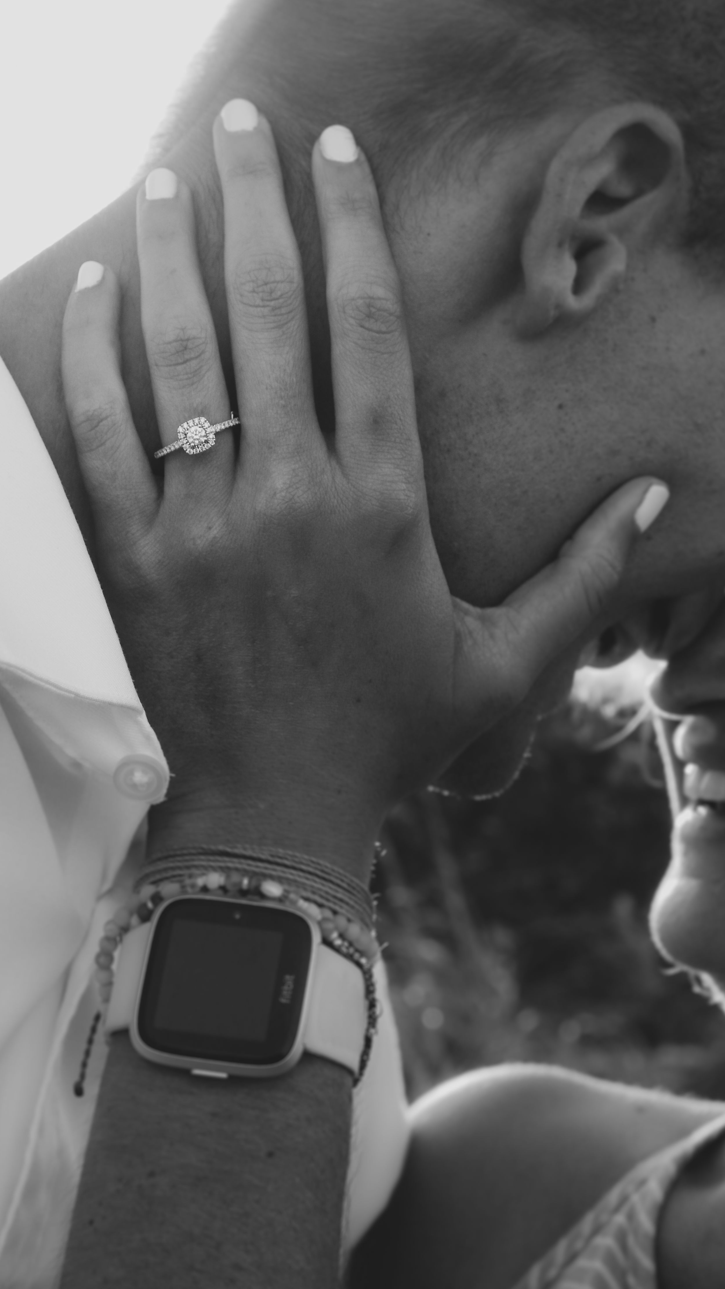 Black and white photo of a couple embracing, showcasing a diamond engagement ring and a smartwatch on the woman's wrist.