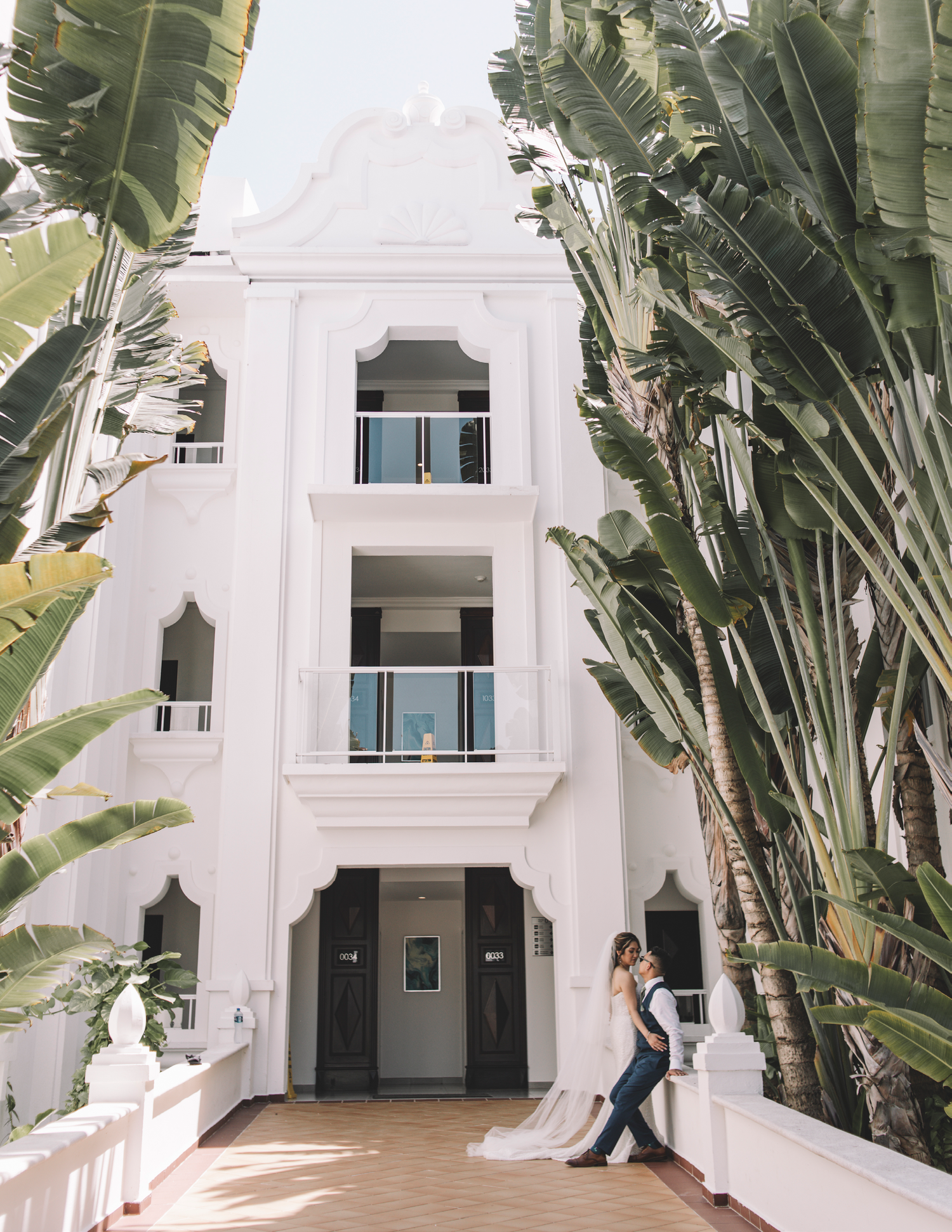 Elegant white building exterior with palm trees and couple embracing on steps.