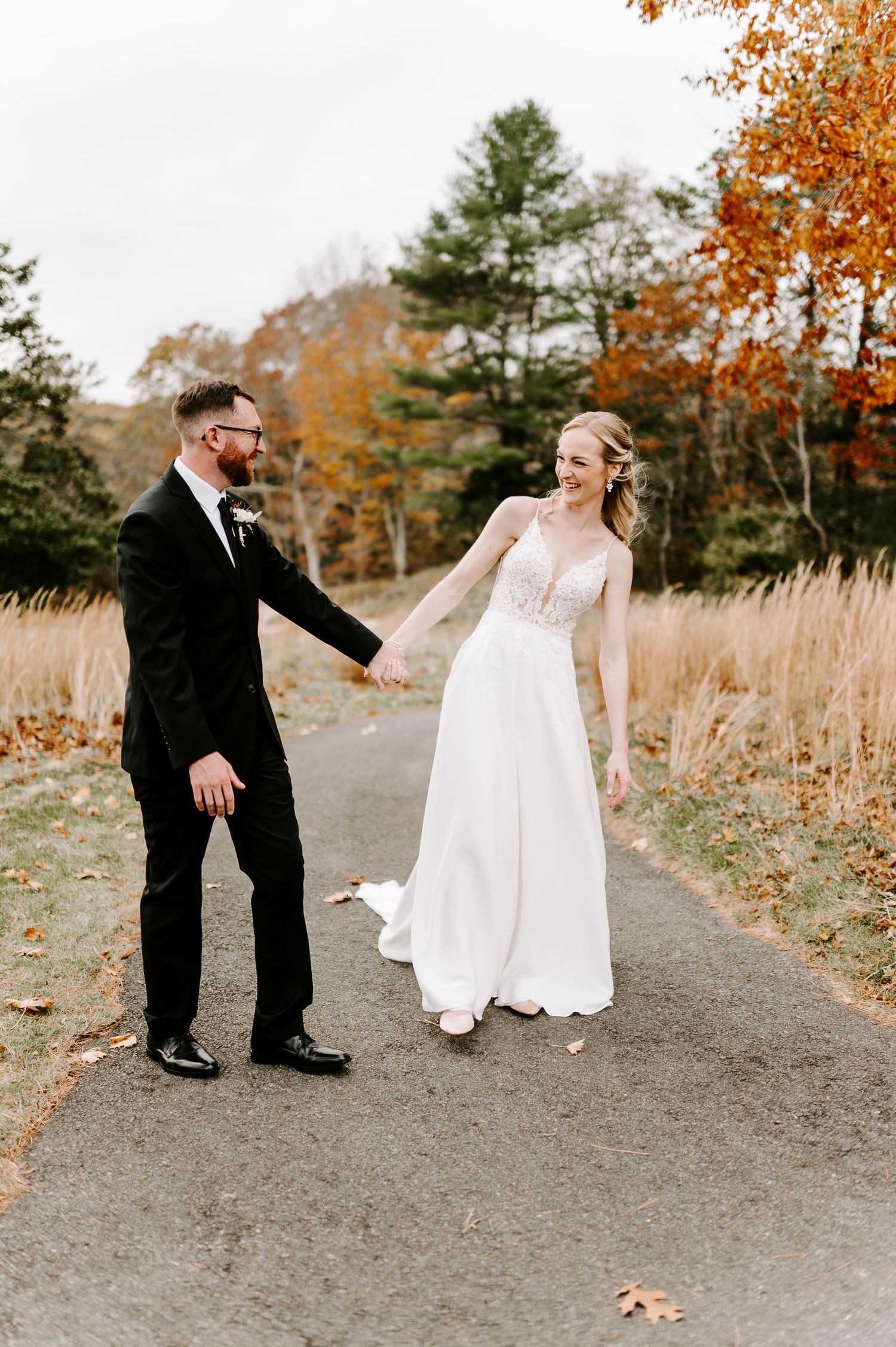 Playful moment between couple on gravel path with autumn foliage.