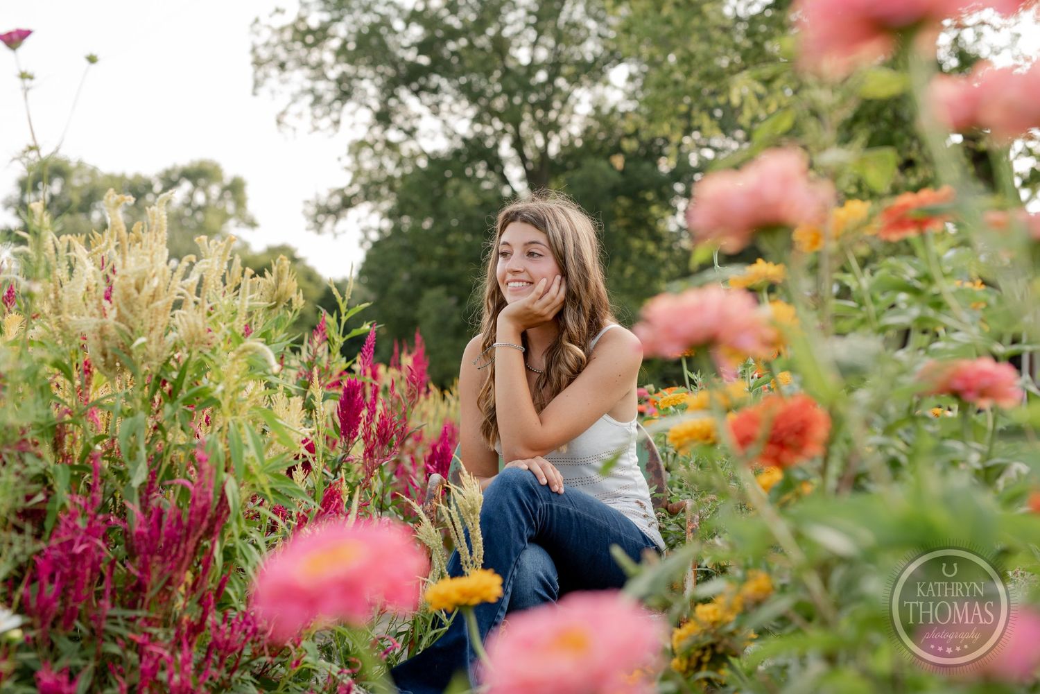 A person sits thoughtfully in a garden surrounded by pink and orange blooms on a summer day.
