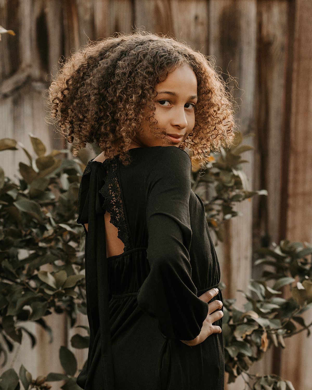 Artistic portrait of someone with natural curly hair wearing black against a wooden backdrop.