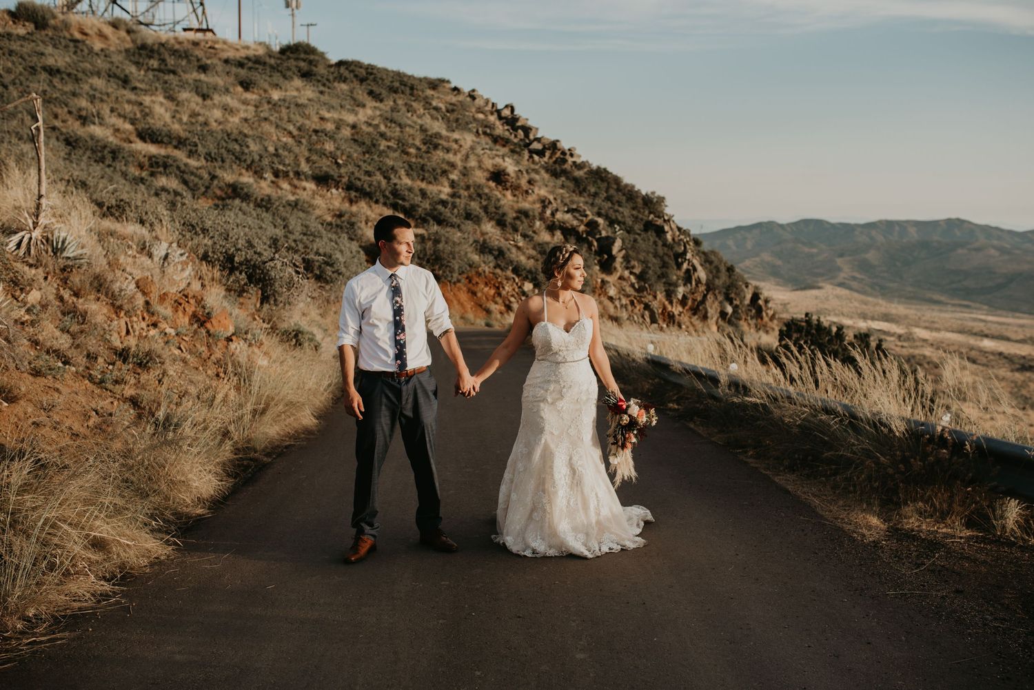 Wedding couple walking along mountain road with scenic desert valley views.