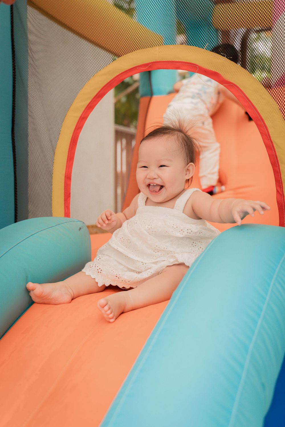 A joyful baby laughing while playing on an orange and blue bouncy castle.