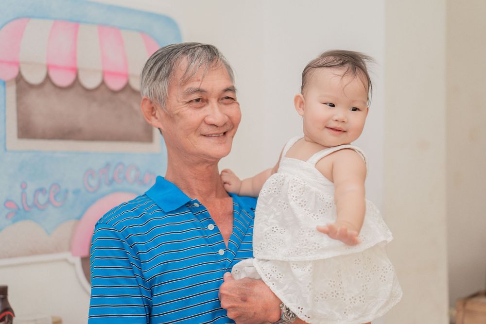 A baby in a white lace dress being held at a festive party with pink decorations.