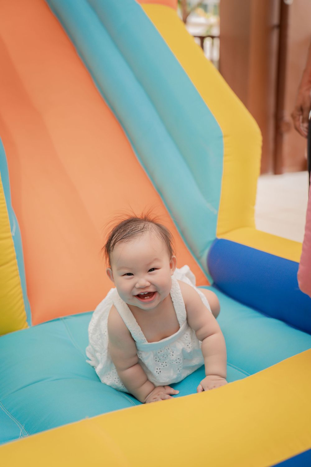 Baby wearing white clothes smiling while playing on a colorful inflatable bouncy castle.