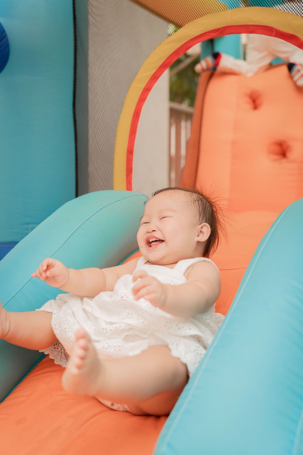 A happy baby lying back on an orange and blue inflatable play structure.