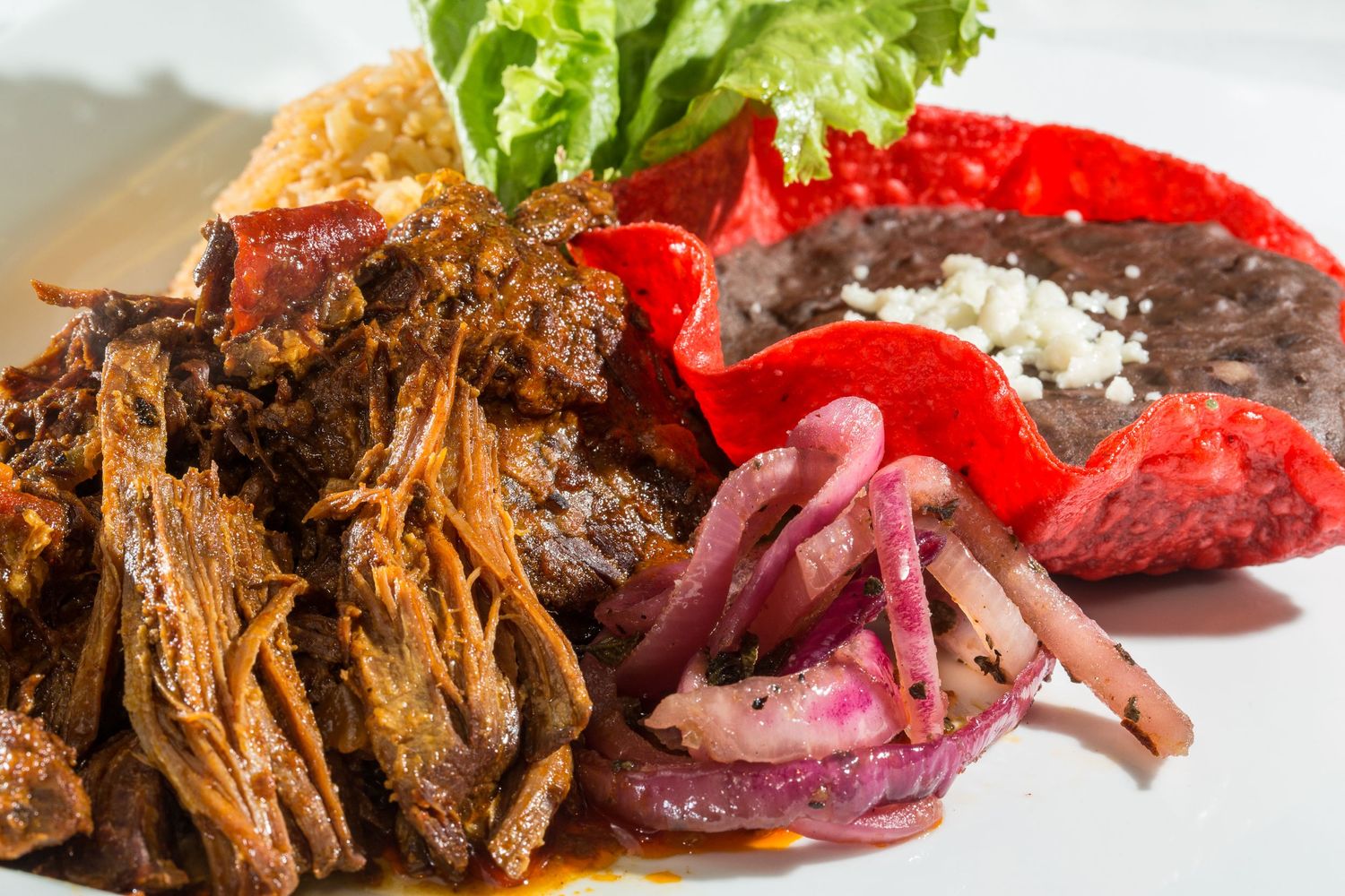 Pulled beef dish served with pickled onions, red peppers, and fresh lettuce.