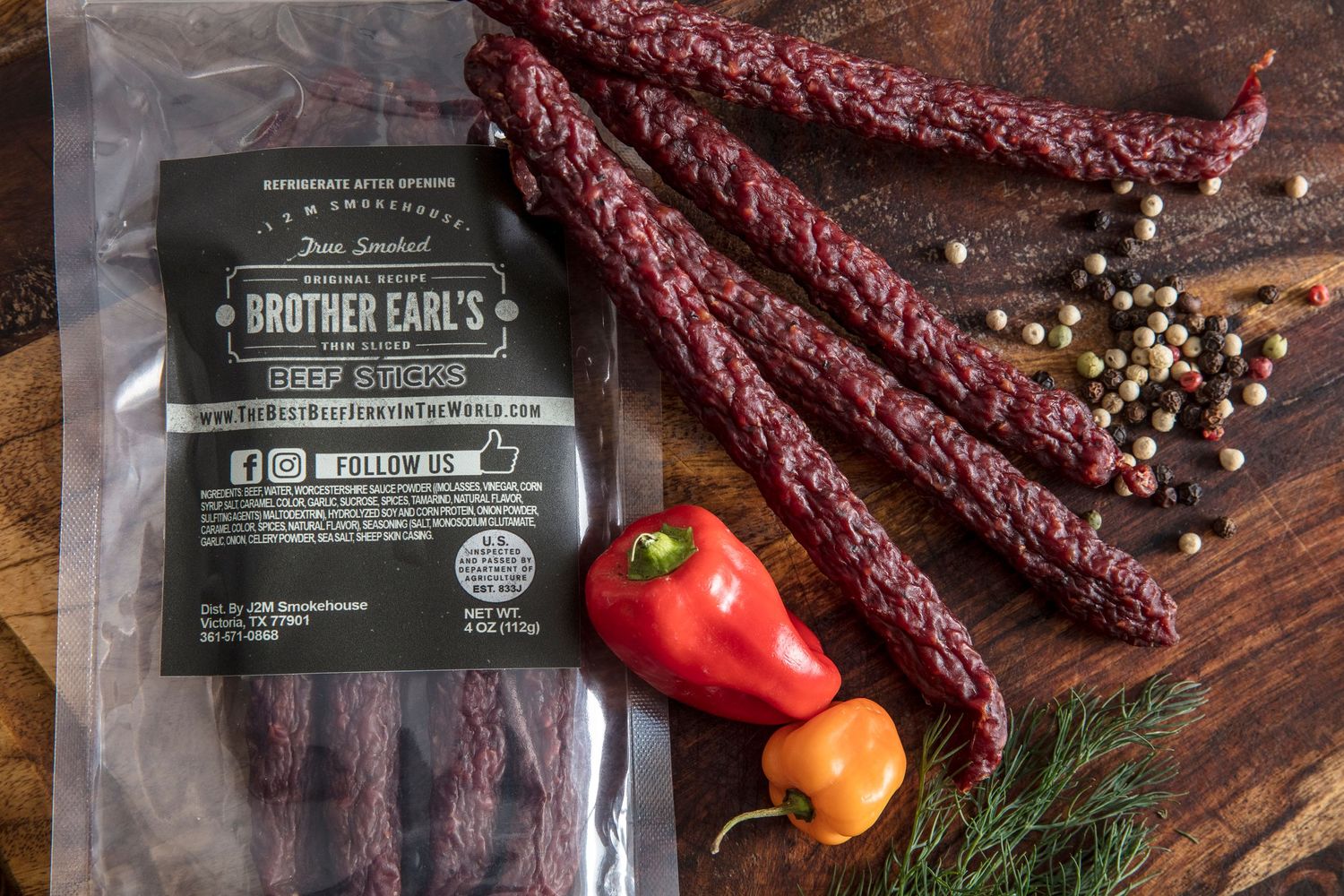 Artisanal beef jerky with fresh peppers and spices on a rustic wooden surface.