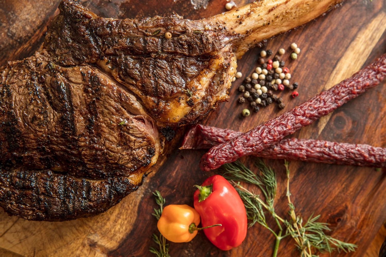 Grilled steak and beef jerky with cherry tomatoes and peppercorns on a wooden cutting board.