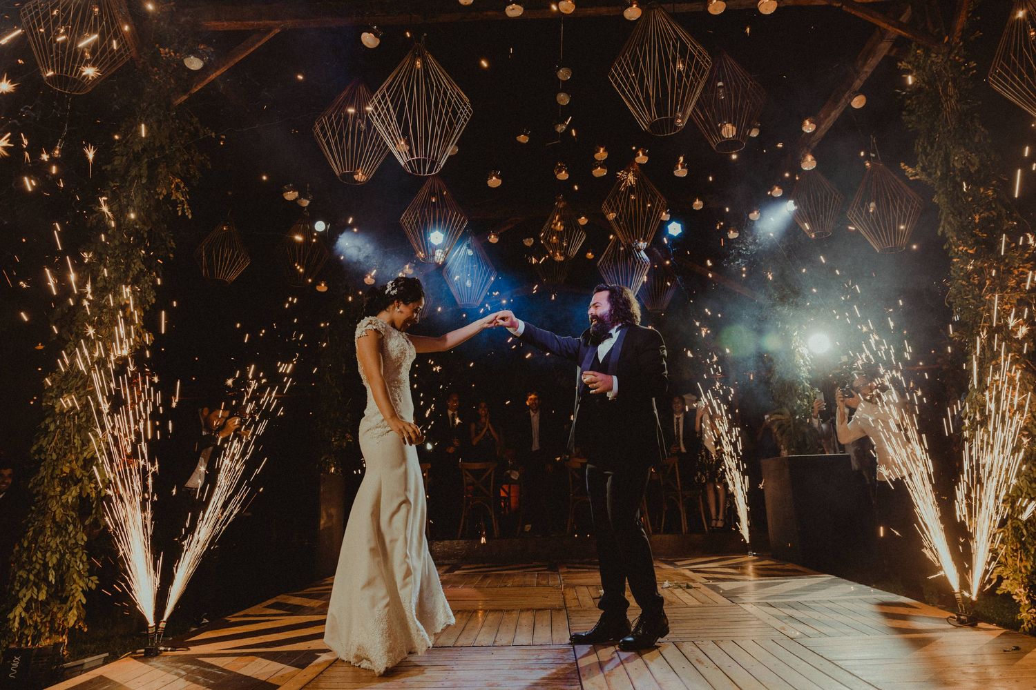 A couple dances under sparklers and hanging lights at an evening wedding reception.