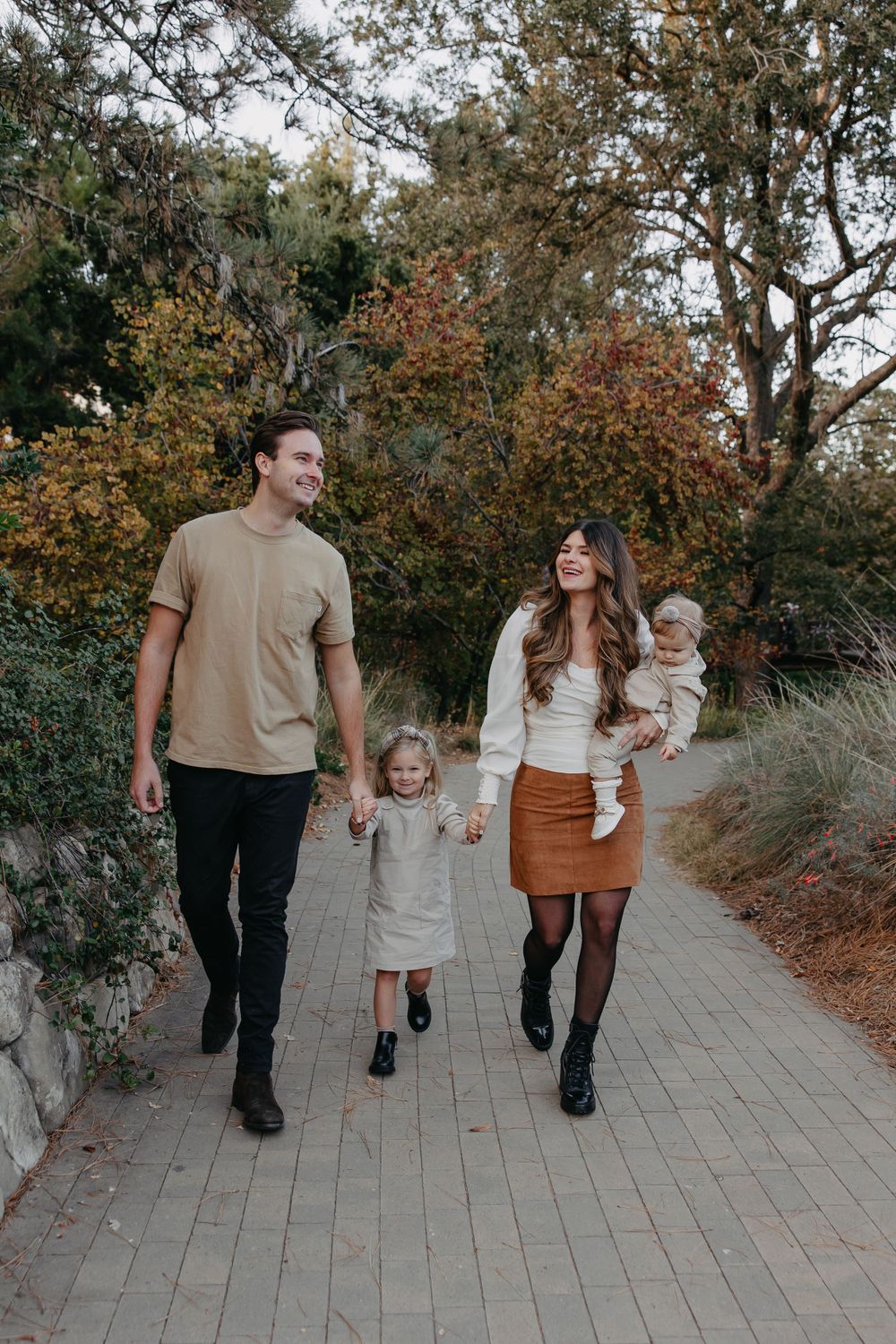 Family walking together on brick pathway surrounded by autumn trees and foliage.