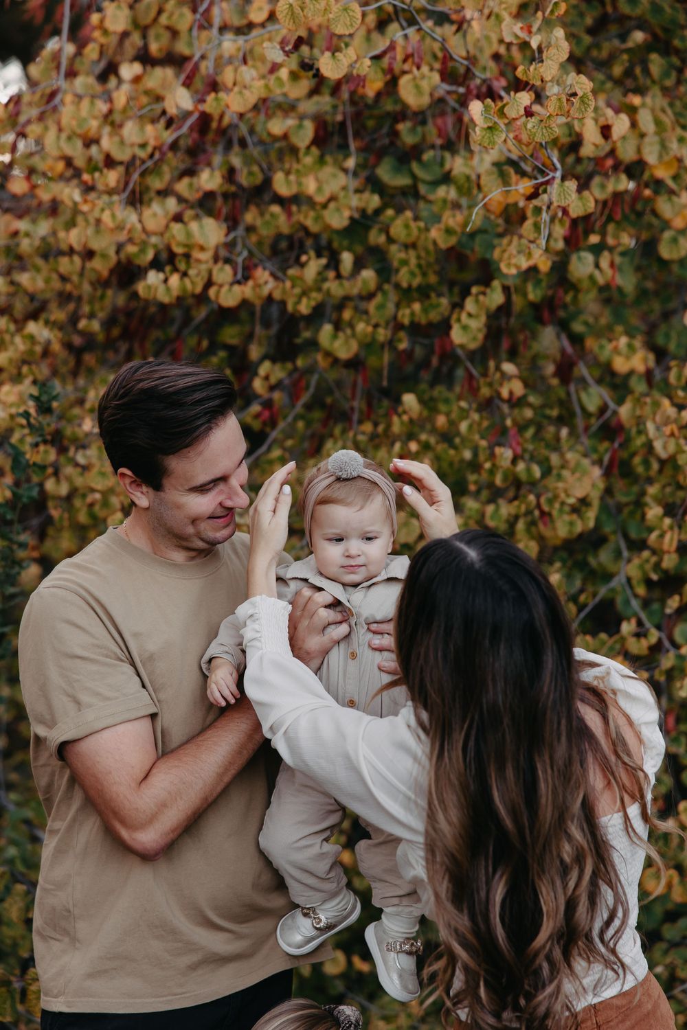 Parents share tender moment with baby in garden setting with fall colors.