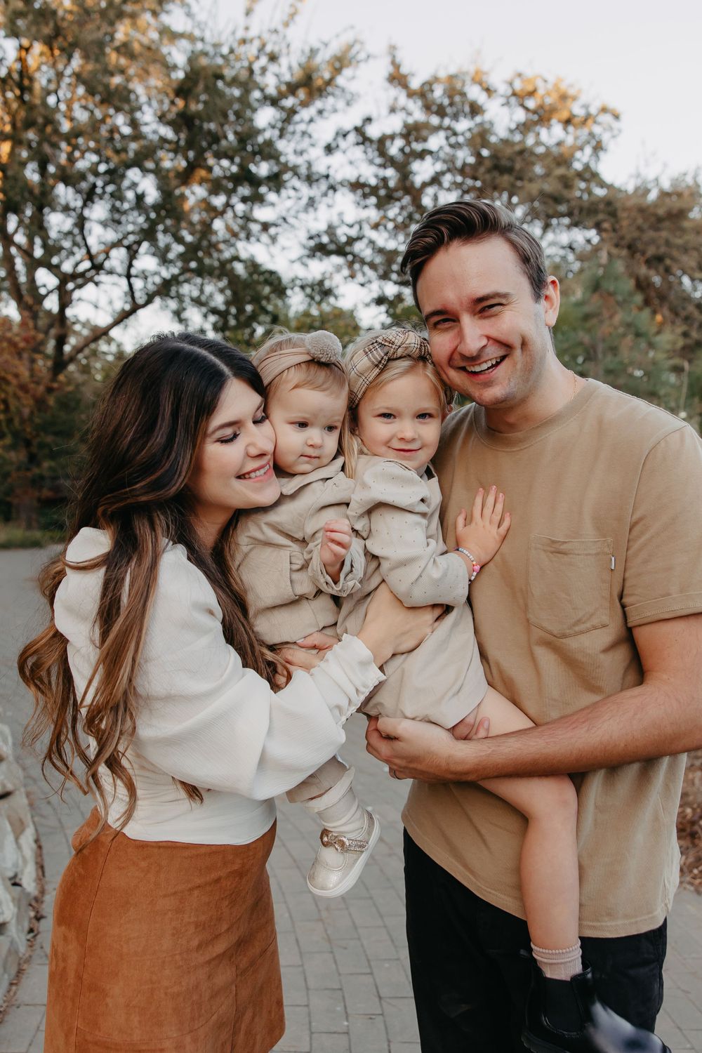 Candid family portrait with coordinated neutral outfits in outdoor autumn setting.