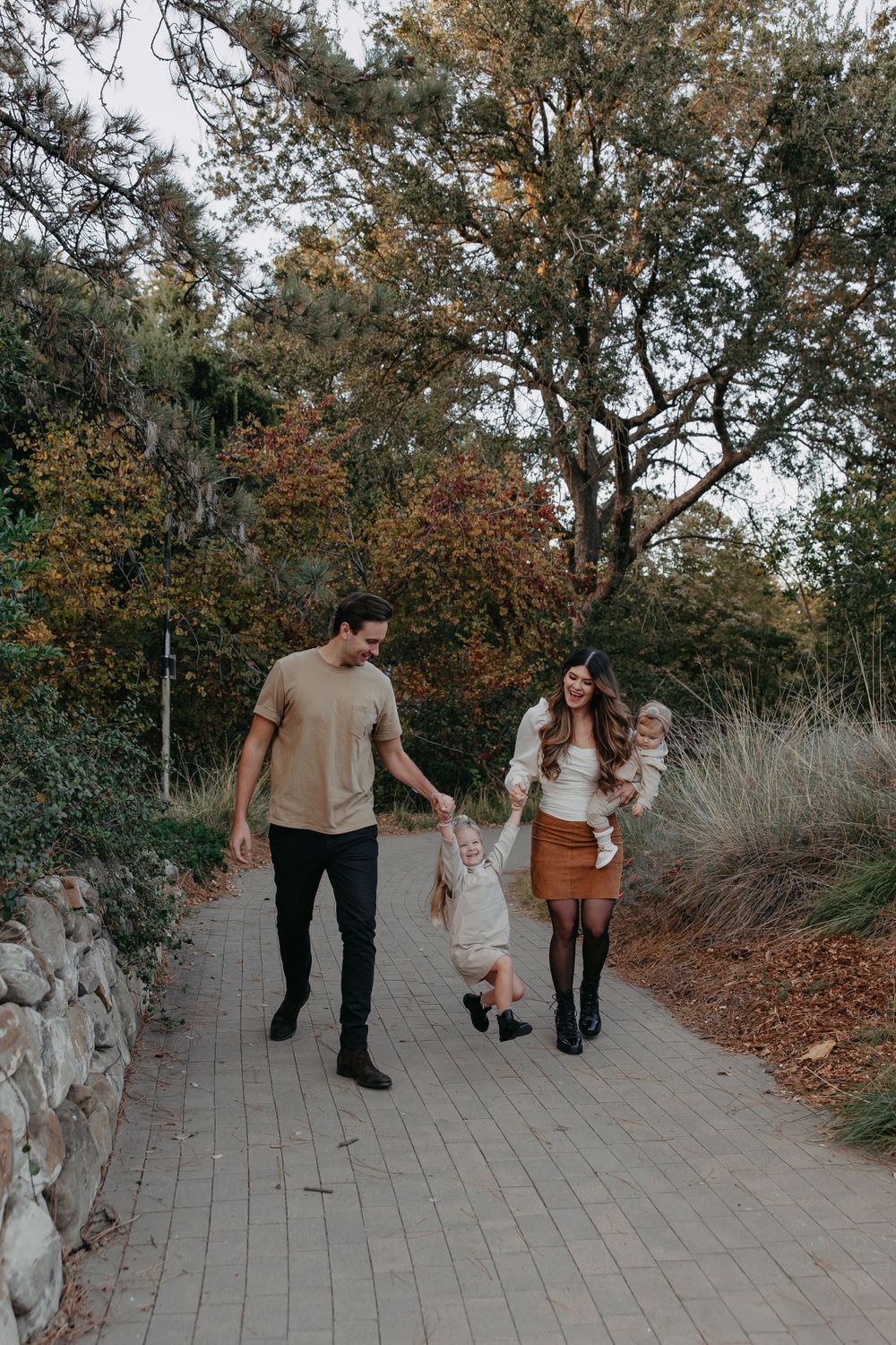 Family taking autumn stroll together on brick walkway lined with trees and stone wall.