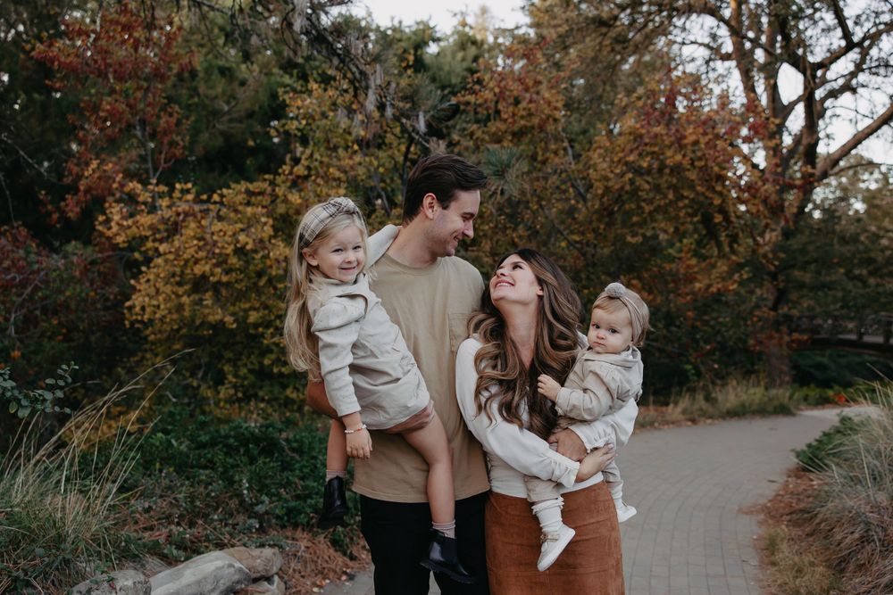 A happy family poses together on a stone pathway surrounded by autumn foliage.