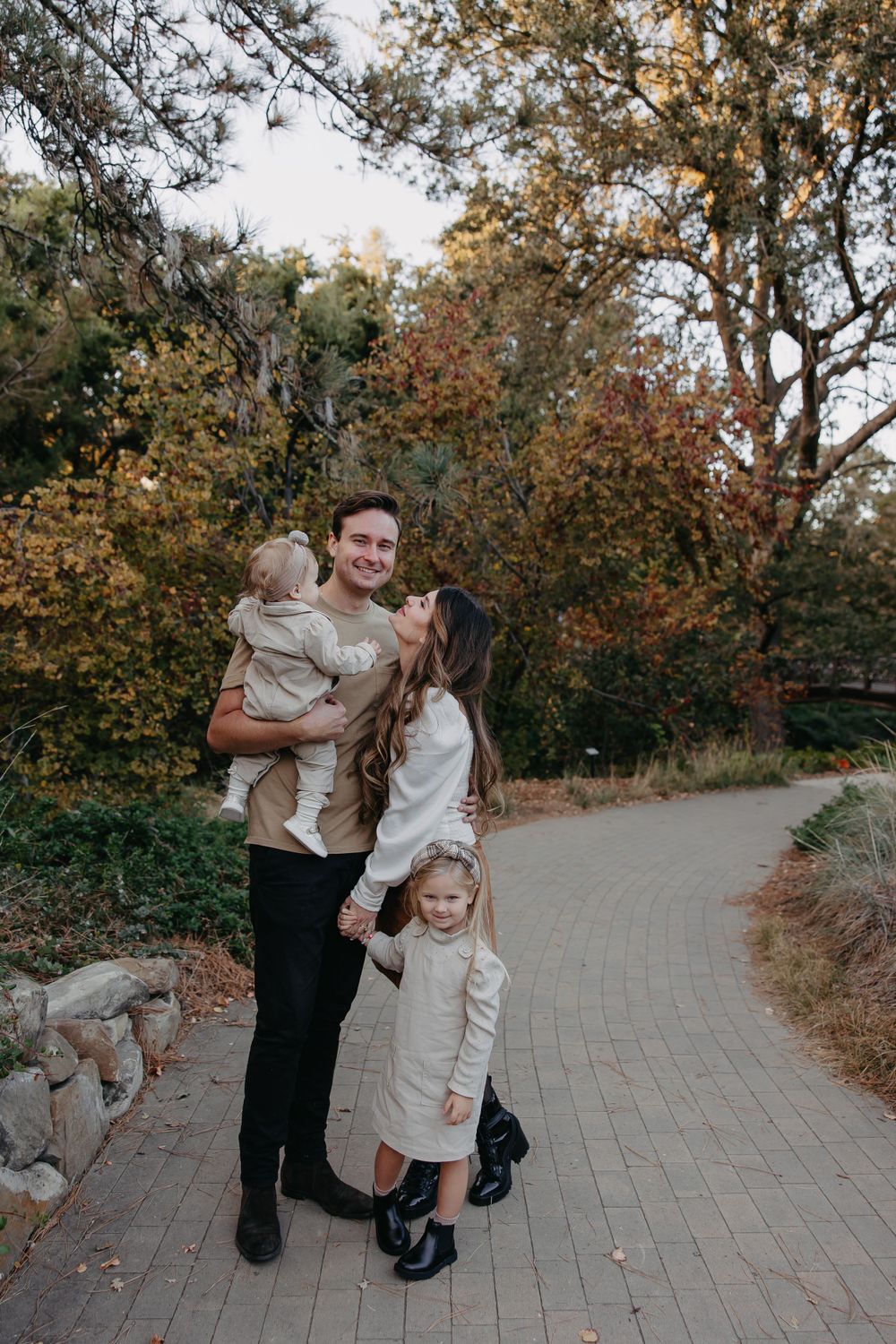 Family of four poses on brick pathway with fall foliage and trees in background.
