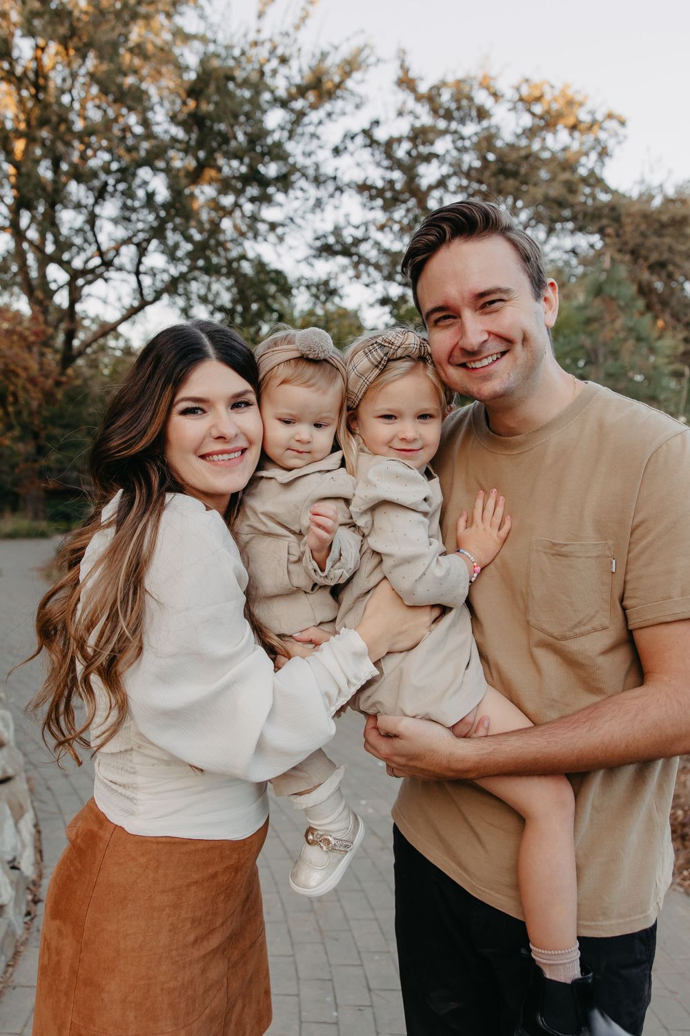 Family portrait outdoors with coordinated neutral outfits against autumn backdrop.