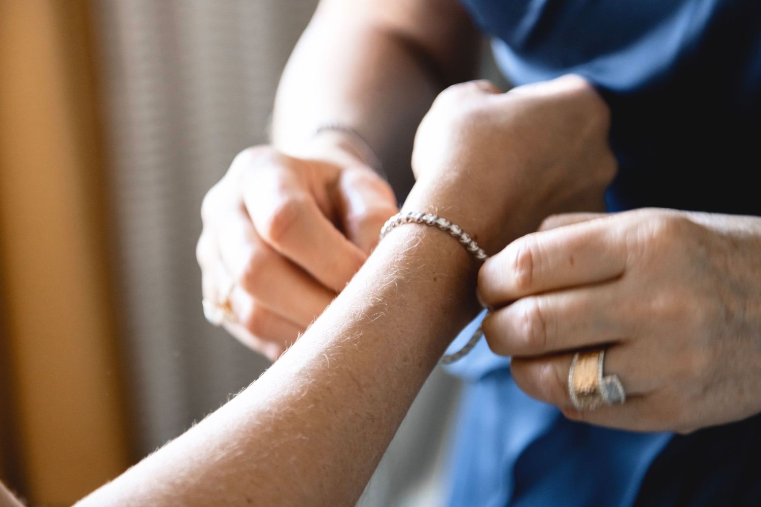 Close up view of hands clasping a delicate silver bracelet around a wrist.