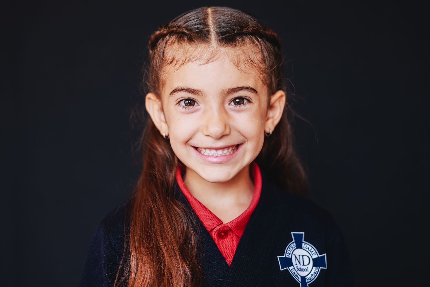 A student in a blue school uniform with red collar poses against a dark background.