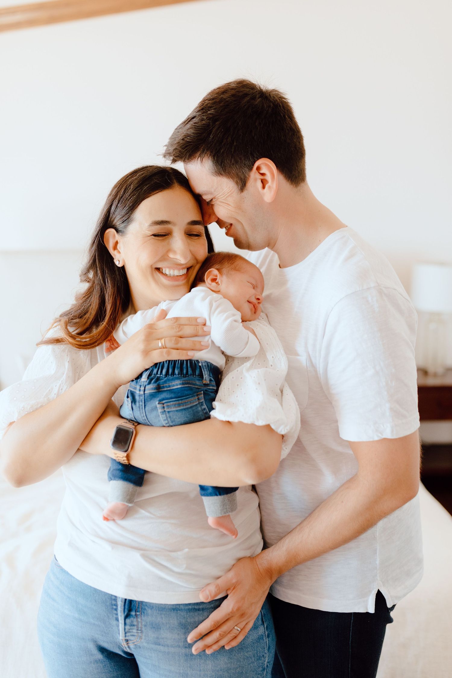 Intimate family moment with baby in white onesie and denim being held by parents in matching white shirts.