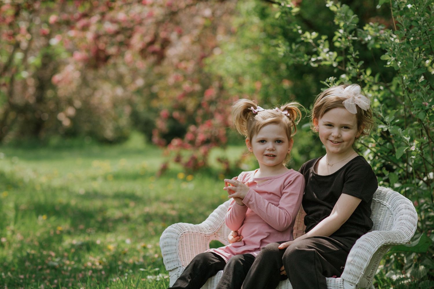 Two people share a quiet moment on a white wicker chair surrounded by spring blossoms.