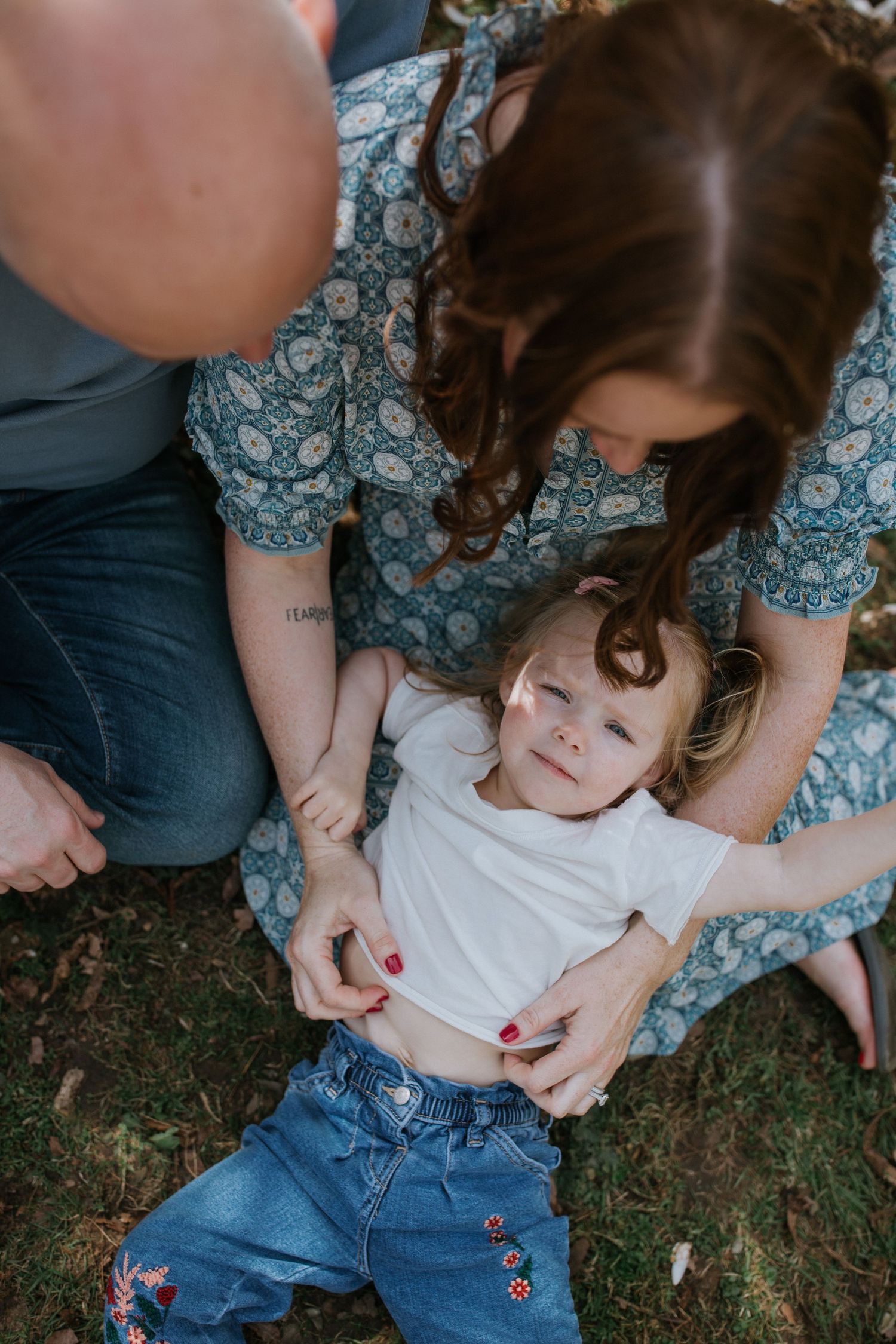 Playful moment captured as parent and child share laughter while laying on grass outdoors.