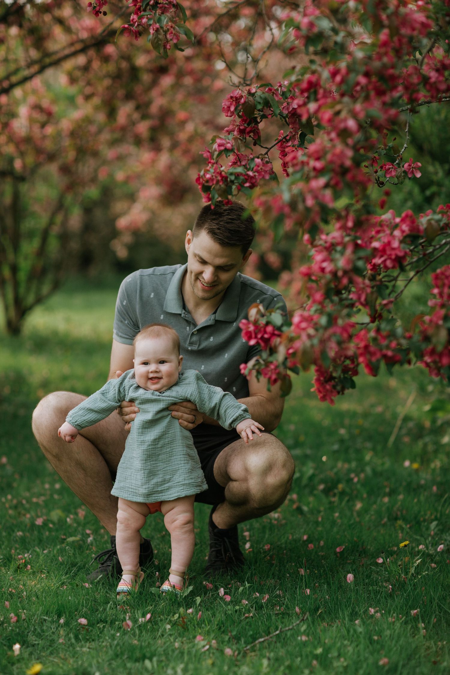 Parent and baby explore blooming pink flowers together in spring garden setting.