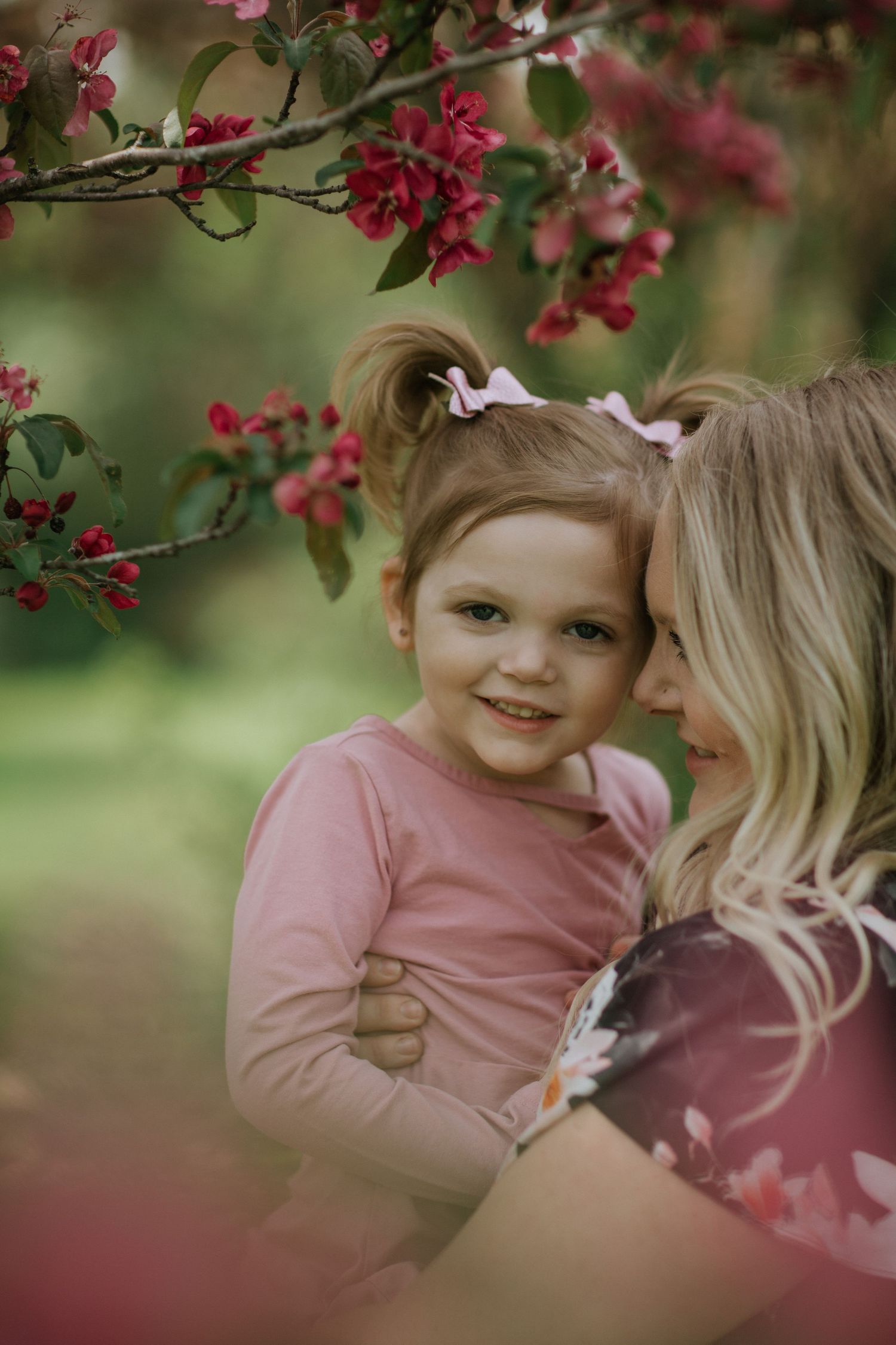 Tender moment between parent and child among blooming pink flowers in garden.