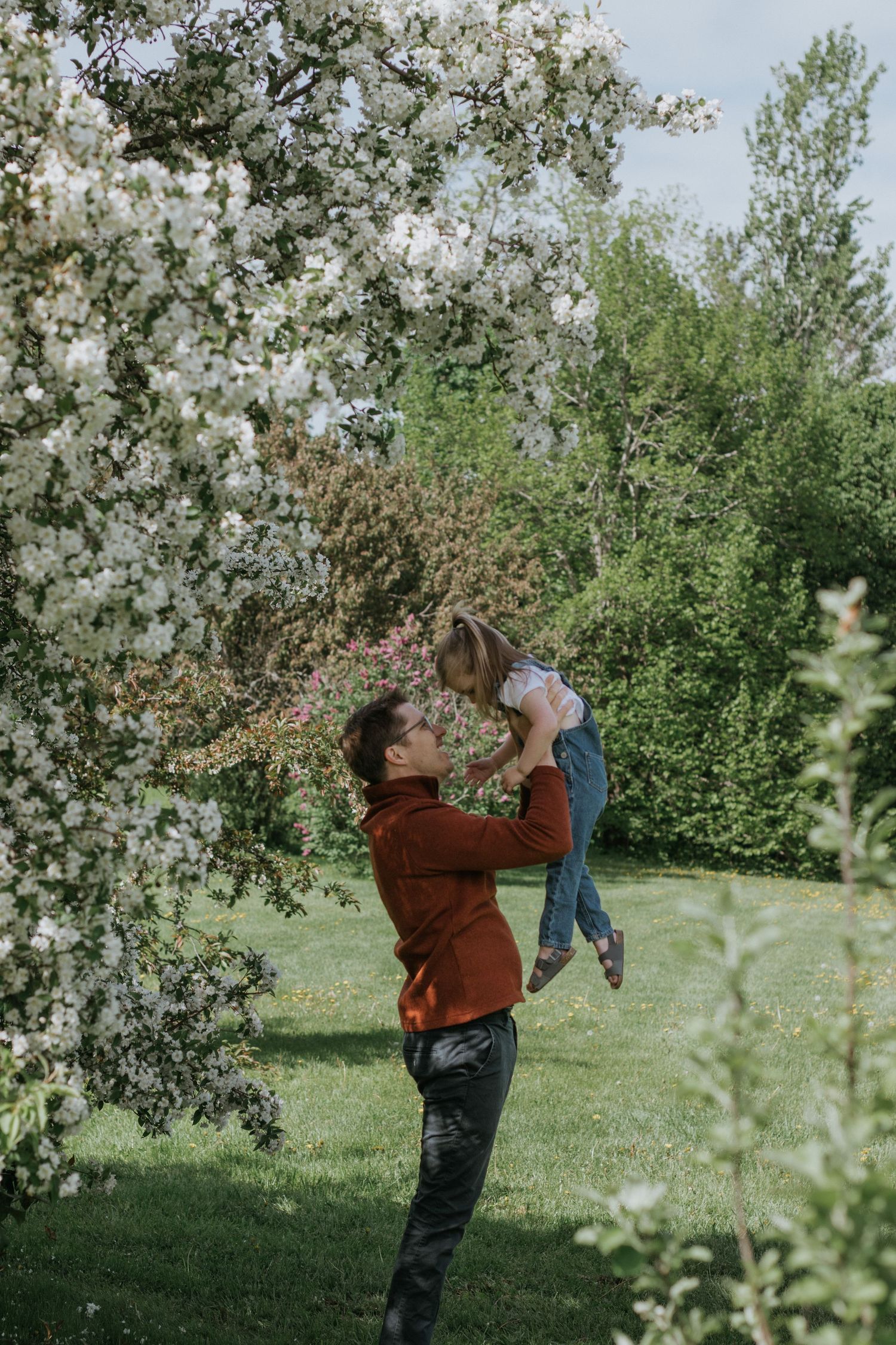 Parent lifting child high in the air under flowering spring tree branches.