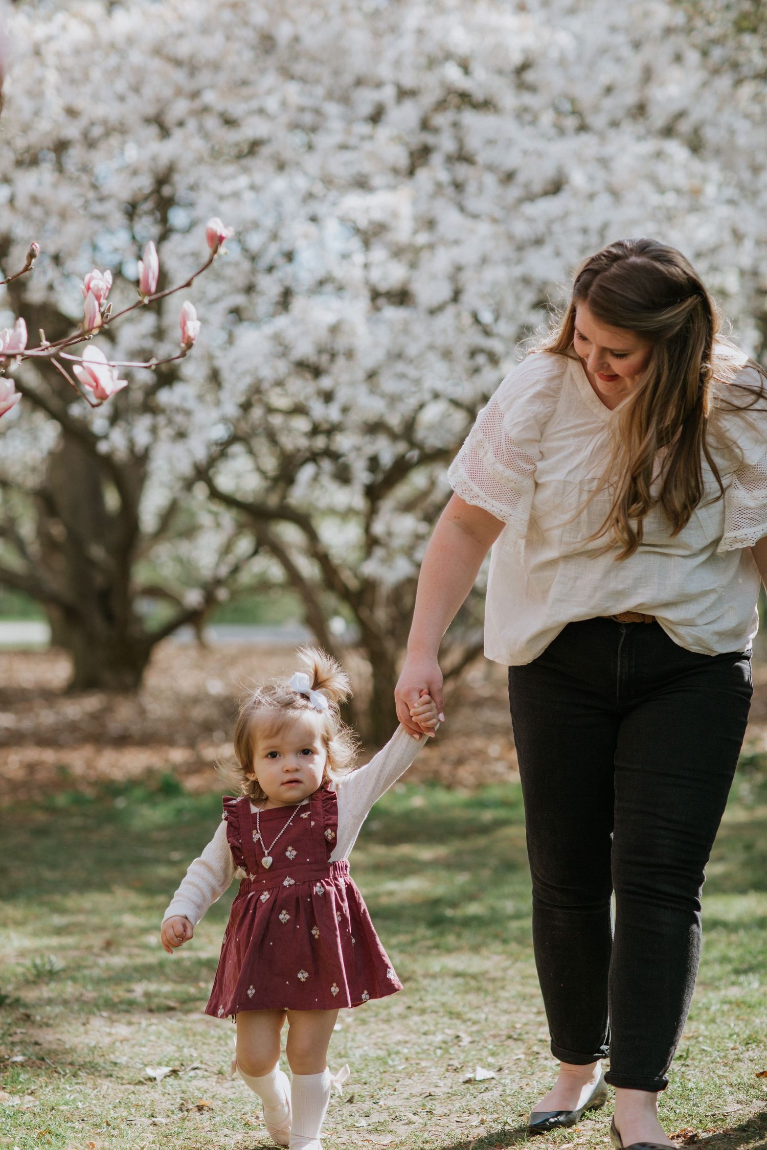 Walking among cherry blossoms while holding hands under blooming spring trees.