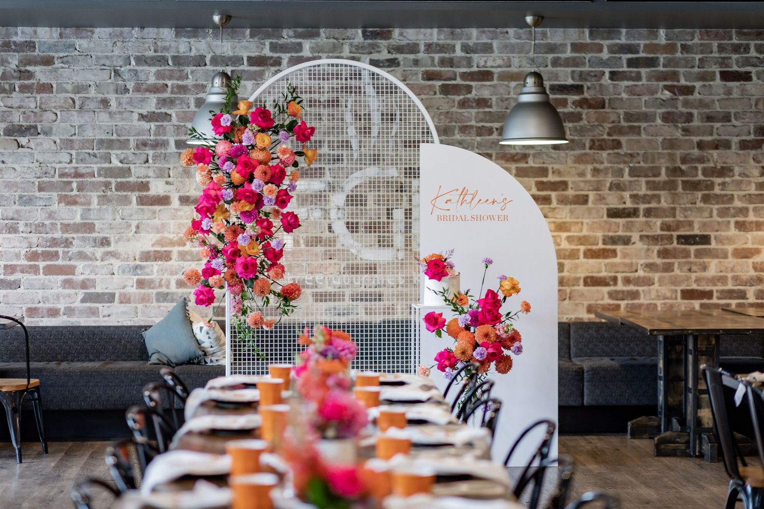 Industrial chic event space with floral decorated white mesh screen and table settings.