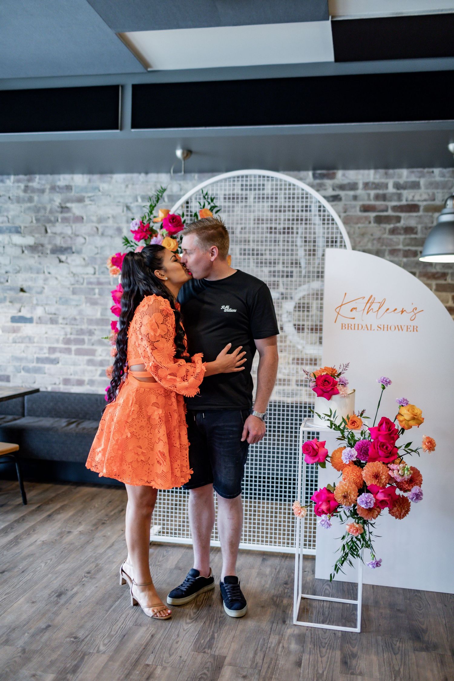 Colorful floral display with pink and orange blooms next to white circular arch at event space.