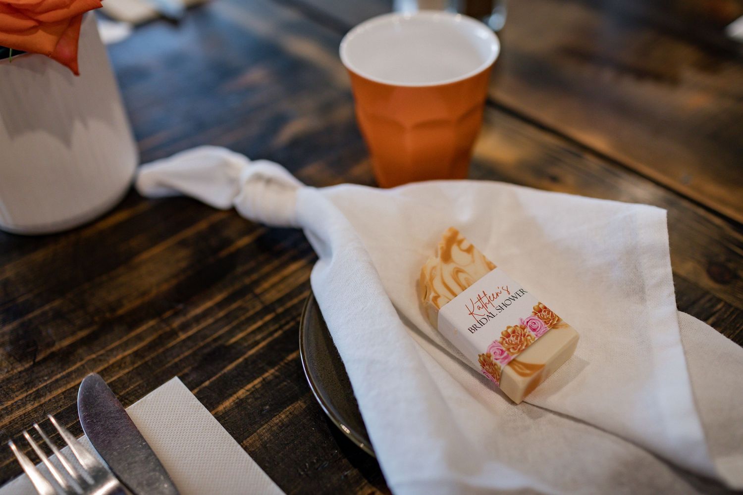 Place setting detail with embroidered napkin and orange cup on rustic wooden table.