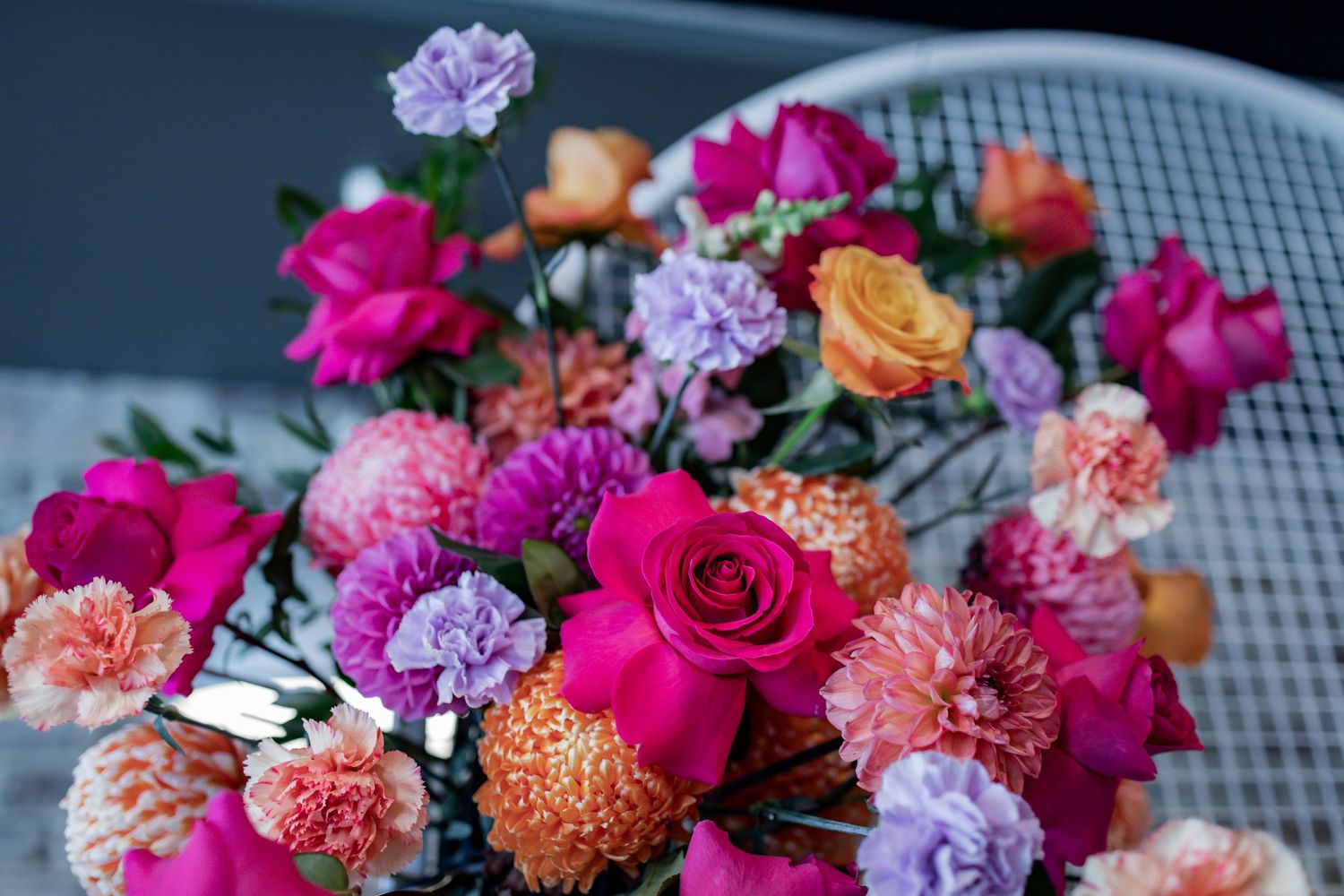 Detailed view of luxurious flower arrangement with fuchsia roses, peach carnations, and purple blooms.