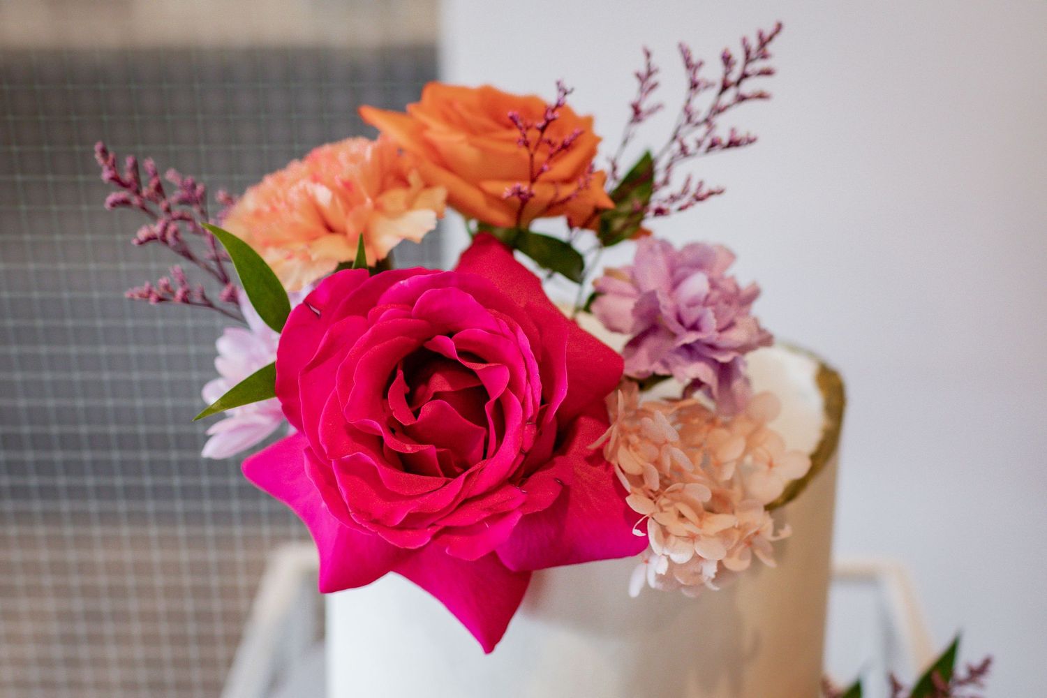 Closeup of bright pink and peach roses with purple accents in a floral arrangement.