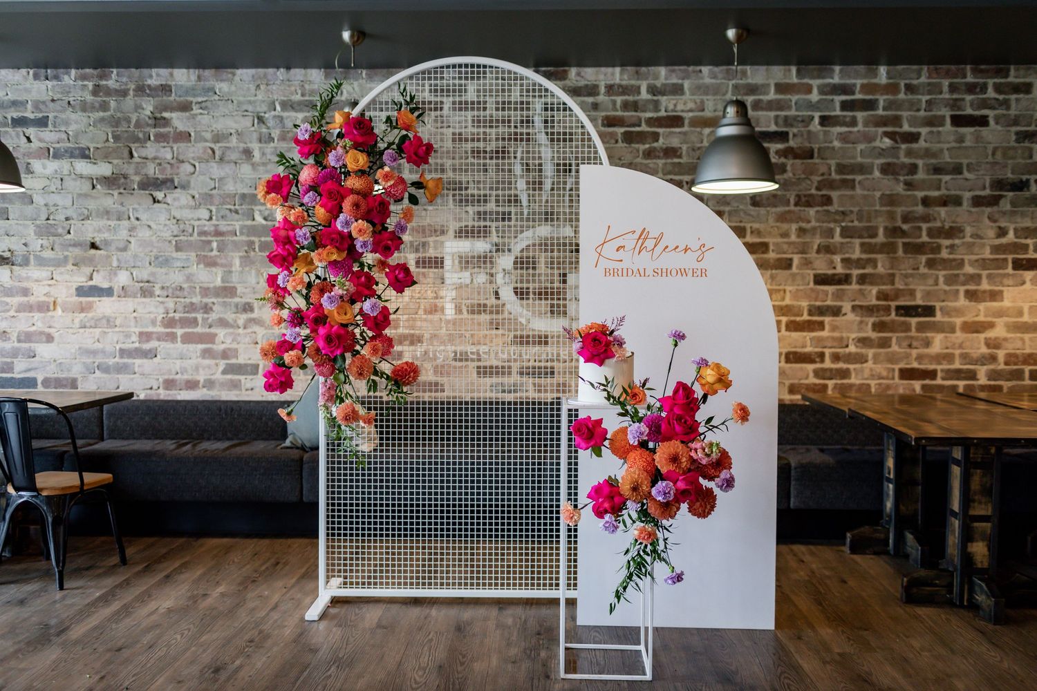 Elegant white arched backdrop with cascading pink and orange flowers in an industrial-style event space.