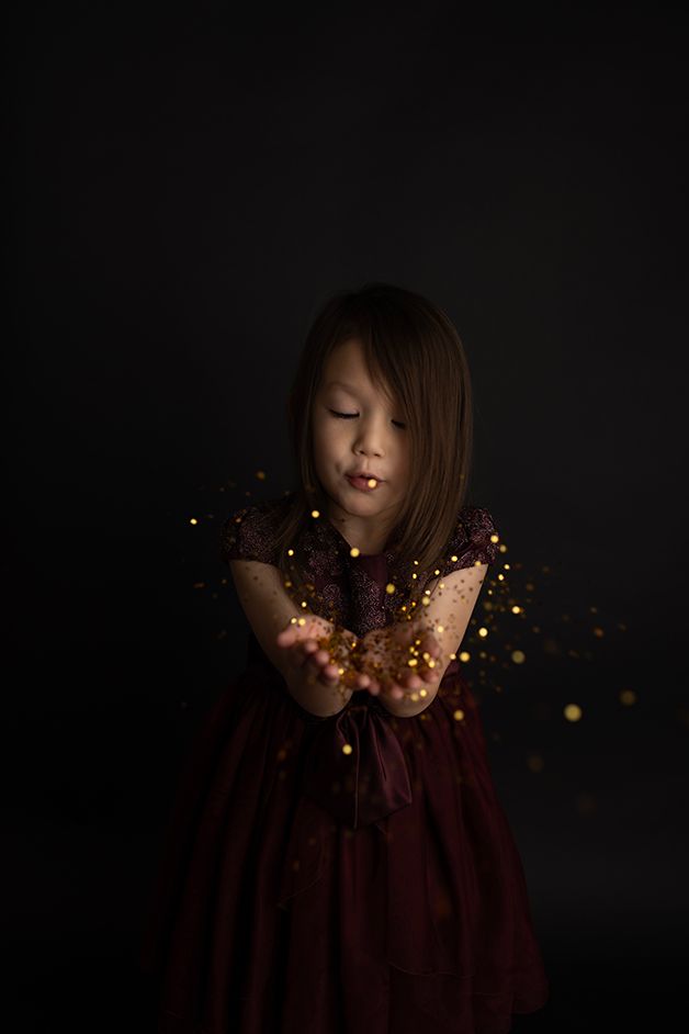 Child blowing gold glitter towards the camera on a black backdrop,.