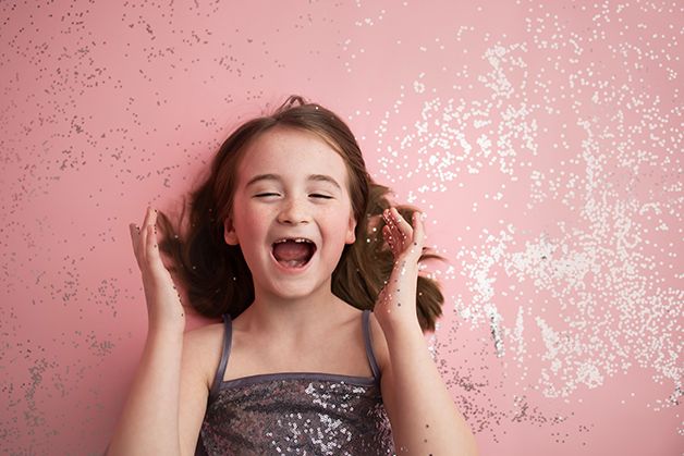 Little girl laying on pink backdrop with silver glitter surrounding her.