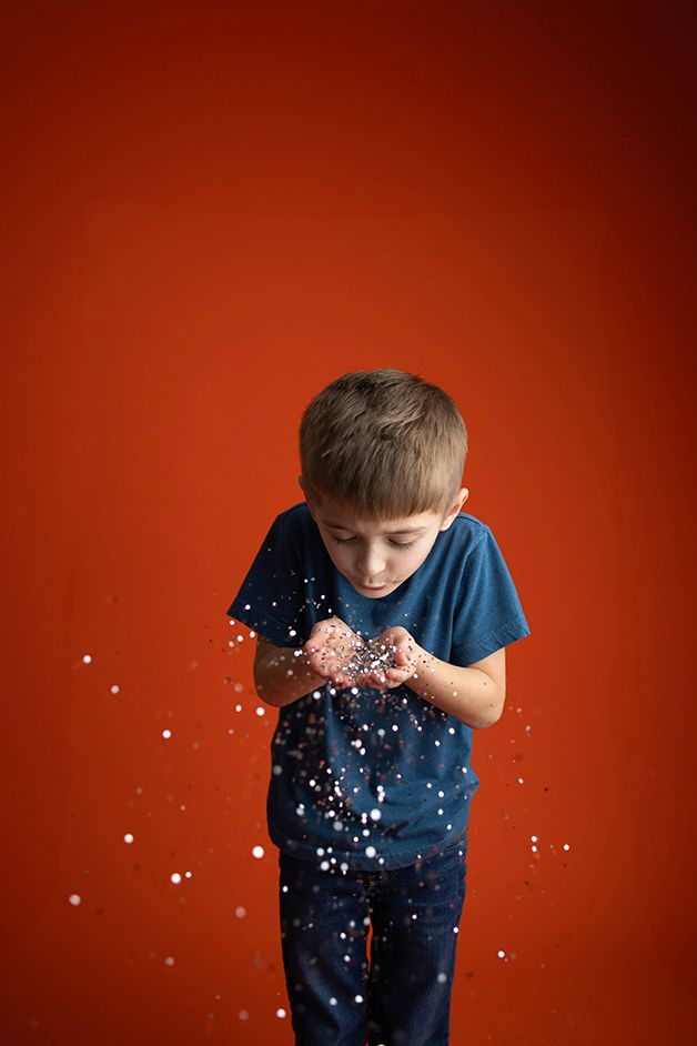 Little boy on a orange backdrop blowing silver glitter.